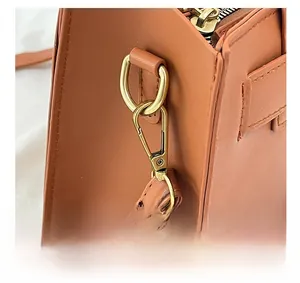 Dettaglio del moschettone dorato e dei componenti metallici su borsa in pelle marrone