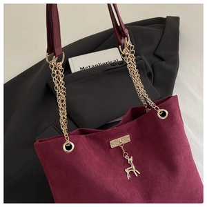 Detail of burgundy suede tote bag featuring a gold chain strap and a deer charm accessory