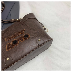 Detail of vintage brown tote bag with fuzzy letter texture and gold metallic hardware