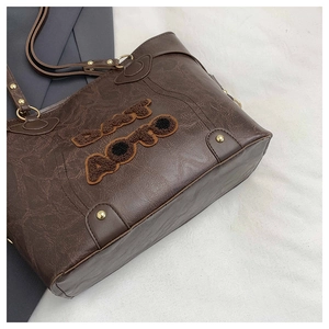 Macro detail of dark brown tote bag with vintage texture and plush letter embroidery