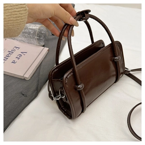 Detail of a deep brown shiny faux leather handbag featuring silver hardware and ball handles