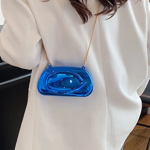 Detail of a bright blue liquid metal clutch with a sleek gold chain on a white suit jacket