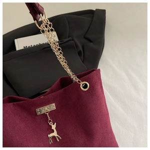 Detail of burgundy suede tote with gold chain strap and elegant deer pendant