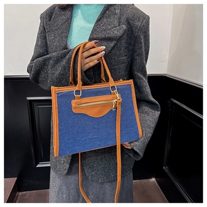 Detail of blue denim tote bag with brown leather trim and golden zipper pocket