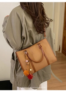 Detail of a brown woven retro handbag with a colorful plush charm worn by a model