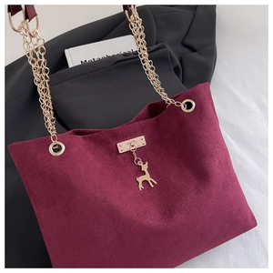 Detail of burgundy suede tote bag featuring a golden deer charm and multi-layer chain strap