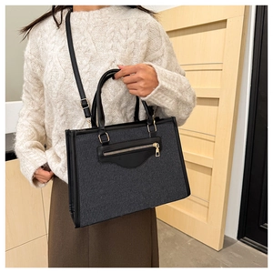 Detalle del bolso tote de lona gris oscuro con adornos de cuero negro y cremallera metálica