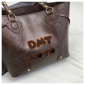 Detail of dark brown tote bag with textured PU leather and embroidered logo patch