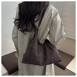 Close-up of a large dark brown suede hobo tote bag worn on the shoulder by a model