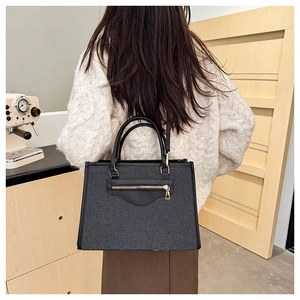 Detalle de bolso tote de tela gris oscuro con detalles en cuero llevado por una modelo