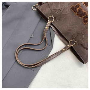 Close-up of vintage brown leather tote bag with plush letter patches and gold metal rings