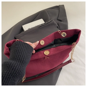 Macro shot showing magnetic closure and gold deer ornament on burgundy velvet tote