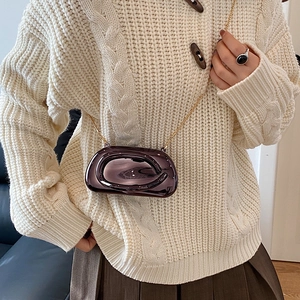 Detail of a purple mirror-finish oval mini bag with gold chain on a knit sweater