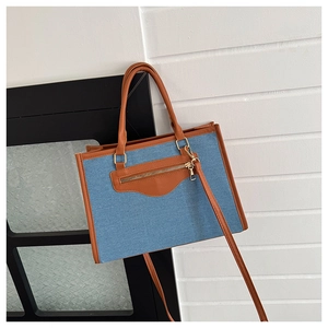 Detail of the blue denim tote bag showing brown leather handles and decorative zipper pocket