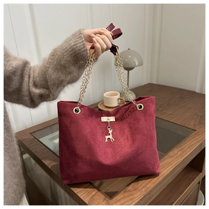 Close-up of wine red suede tote bag featuring gold chain and deer charm detail