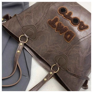 Detailed close-up of dark brown tote bag with fuzzy CLOA DWLI letters and gold hardware