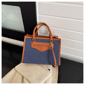 Detail of denim and leather tote bag with contrasting caramel trim and gold zipper