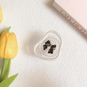 Close-up of heart-shaped cream hair claw clip with black polka dot bow on white surface