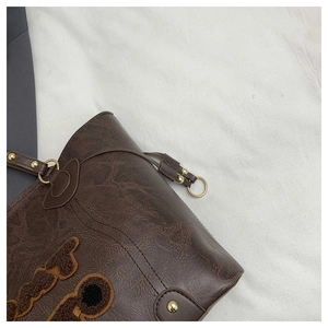 Detail of vintage brown leather bag featuring plush letter patch and gold rivets