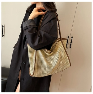 Detail of a woven tote bag with brown leather trim and contrast strap on shoulder