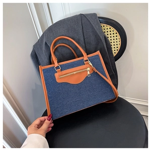Close-up of retro denim and brown leather tote bag displayed on a black chair