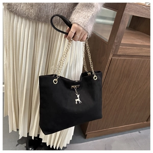 Detail of black suede tote bag featuring a gold deer charm and chain shoulder strap