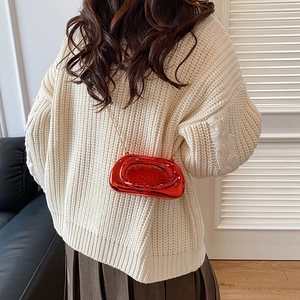 Detail view of a bright red sculptural chain bag with high-gloss finish on a female model