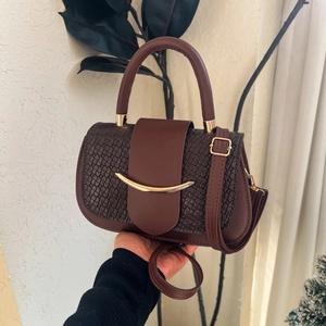 Detail of a brown woven leather crossbody bag with a golden arc buckle and top handle