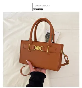 Detail view of a brown handbag with a heart-shaped gold buckle on a white fabric background