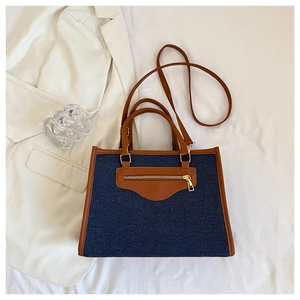 Detalle del bolso tote de denim azul y cuero marrón con costuras en contraste