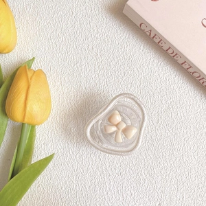Detail view of a wavy clear acrylic hair claw clip with a cream bow on a soft white cloth