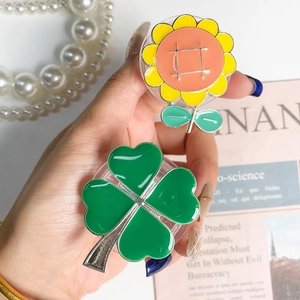 Detail of collapsible phone grip with yellow sunflower and green clover enamel designs
