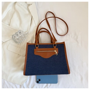 Detailed top view of denim and brown leather tote bag with metal zipper and strap