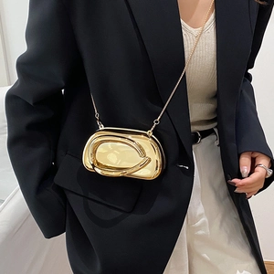 Close-up of golden metallic oval clutch bag with thin chain strap on black suit
