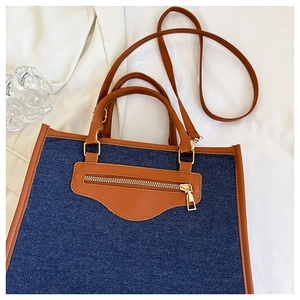 Close-up of blue denim tote bag with brown leather trim and golden metal hardware