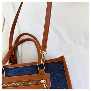 Detail of blue denim tote bag featuring brown leather trim and golden metal zipper pocket