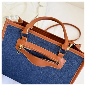 Close-up of contrast denim tote bag with brown leather handles and gold zippers