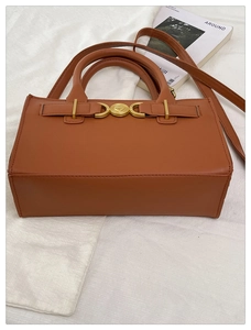 Dettaglio ravvicinato di borsa in pelle marrone con chiusura a cuore dorata su una rivista