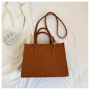Detail view of a vintage brown leather tote bag with gold hardware on white fabric