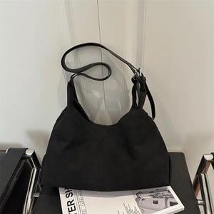 Minimalist black matte hobo tote bag with wide strap on a modern designer chair