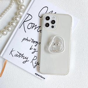 Transparente iPhone-Hülle mit cremefarbenem Bären-Pop-Socket auf weißem Buchhintergrund