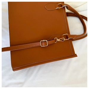 Detail of caramel leather tote bag showing handle attachments and gold metal buckle