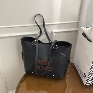Large black tote bag with brown plush embroidery and gold hardware on a table