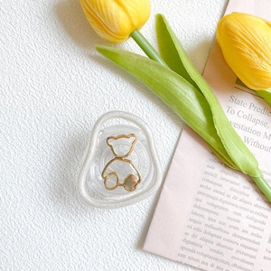 Detail einer transparenten Handyhalterung mit goldenem Bärenrahmen auf weißem Grund