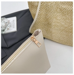 Close-up of a white leather zipper pouch with gold metal puller next to a straw tote bag
