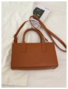 Borsa a tracolla marrone caramello su lino bianco con una rivista in stile minimalista