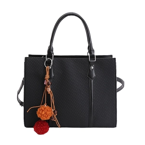 Black twill tote bag with rigid handles and a colorful plush charm on white background