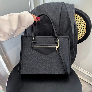 Grey denim tote bag with black leather trim and gold hardware on a chair