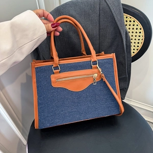 Denim and brown leather tote bag with gold zippers shown in a stylish lifestyle setting