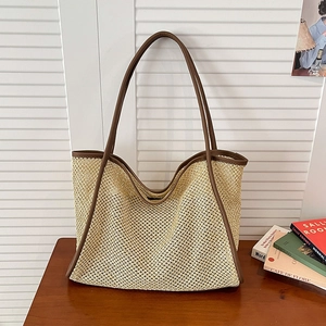 Minimalist woven straw tote bag with brown leather handles on a wooden table surface